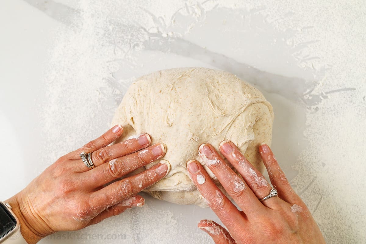 two hands making bread on a floured surface