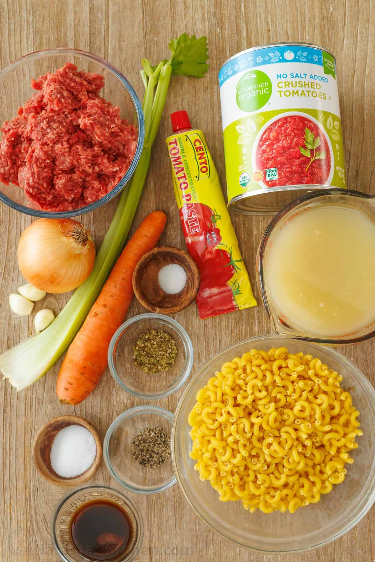 Ingredients for American Goulash recipe including ground beef, crushed tomatoes, tomato paste, celery, carrots, onion, chicken stock, salt, pepper, oregano, elbow macaroni pasta, and Worcestershire