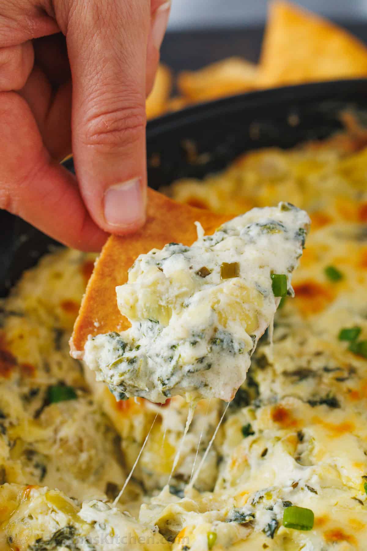 Cheesy spinach and artichoke dip scooped onto a chip with cheese pulls