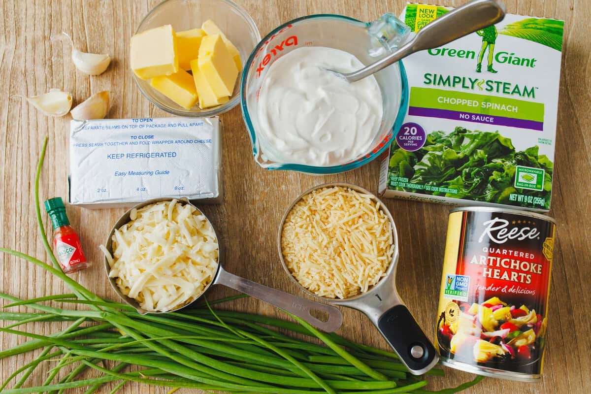 Ingredients to make Spinach and Artichoke Dip, butter, green onions, artichoke hearts, cream cheese, sour cream, chopped spinach, parmesan, mozzarella cheese, garlic, hot sauce, salt