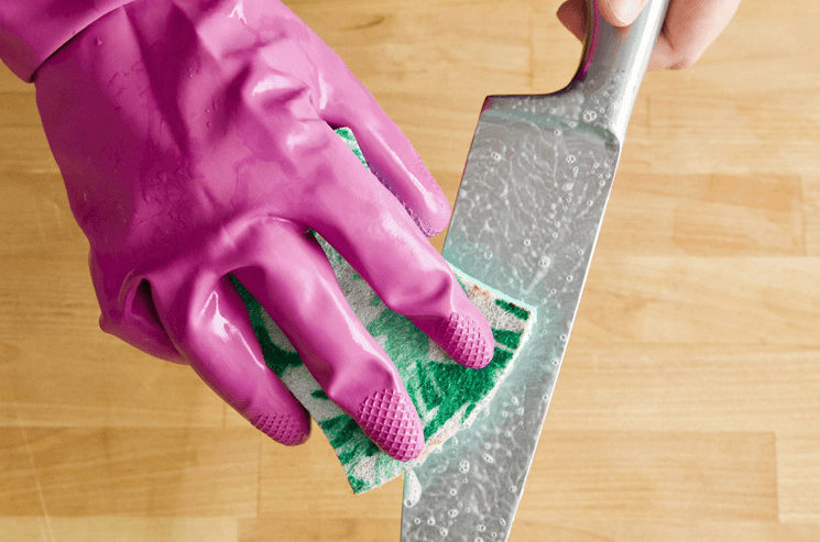 A gloved hand using Bar Keepers Friend and a sponge to clean a cutting knife