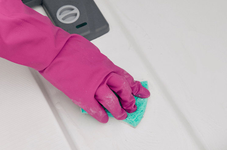 A gloved hand cleaning the inside of a dishwasher using a sponge and Bar Keepers Friend