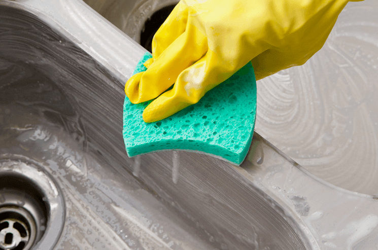 A gloved hand using Bar Keepers Friend and a sponge to clean a stainless steel sink