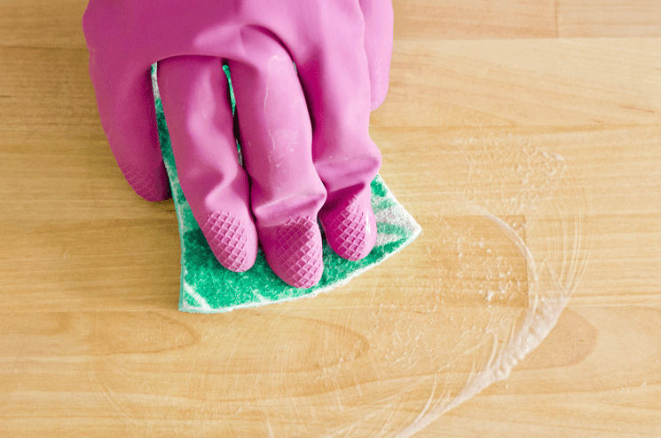 A gloved hand wiping a butcher block countertop with Bar Keepers Friend and a sponge