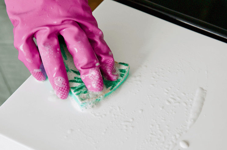 A gloved hand wiping down a white countertop using a sponge and Bar Keepers Friend