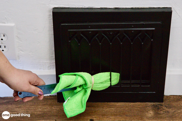 woman's hand using a ruler wrapped in a microfiber cloth to dust a vent grill