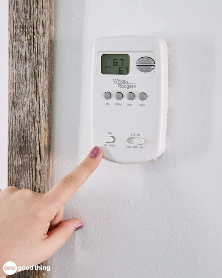 woman's hand using thermostat to turn fan on