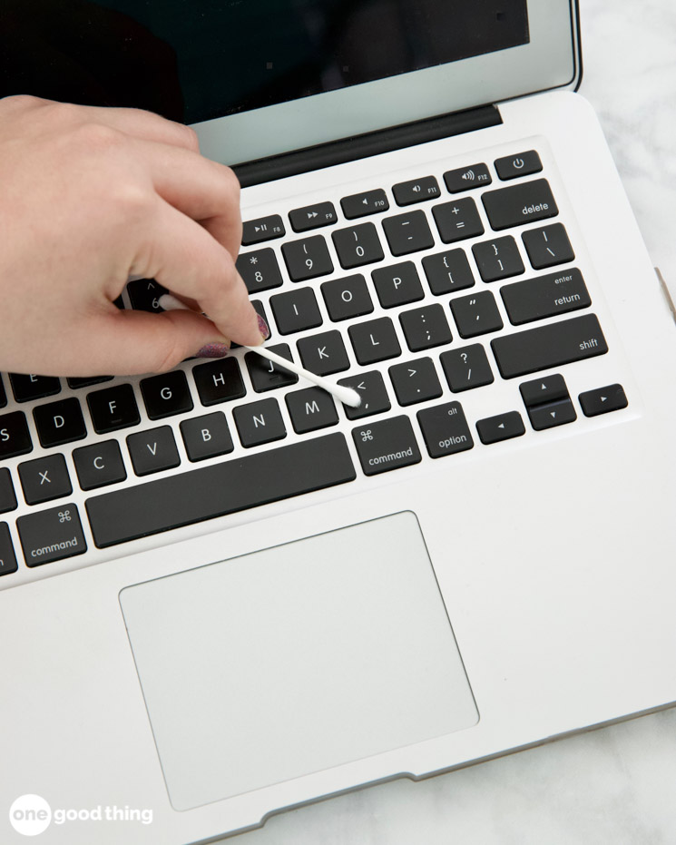 hand using a cotton swab to clean the keyboard of a laptop computer