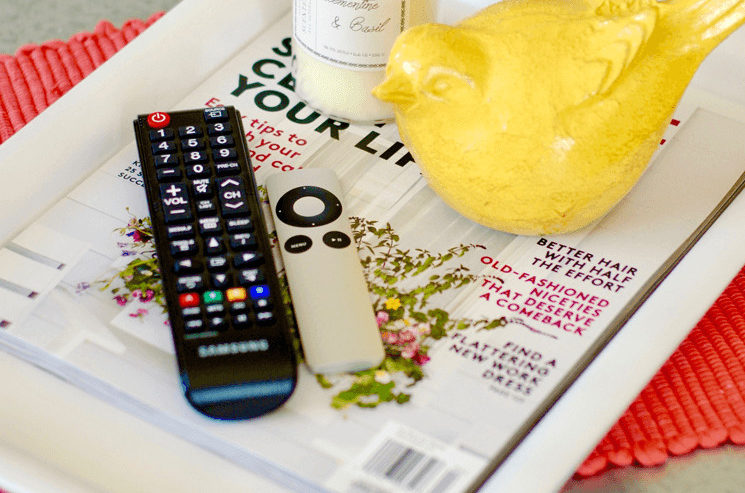 remotes sitting on a tray with magazines and a candle