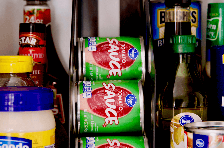 cans of tomato sauce organized in a cabinet shelf with various other food sitting around 