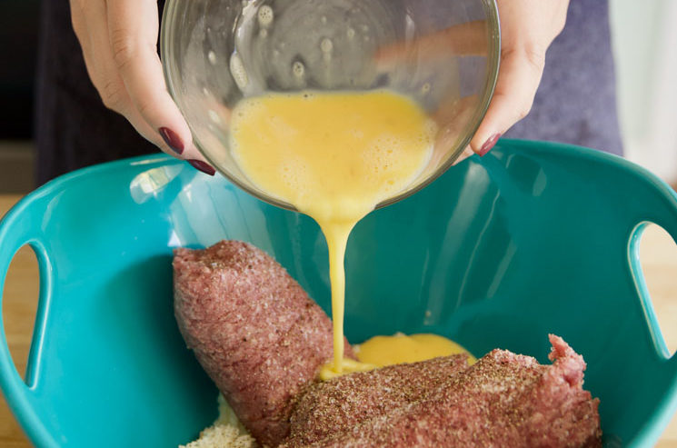 hands pouring beaten eggs into meatloaf mixture in blue bowl