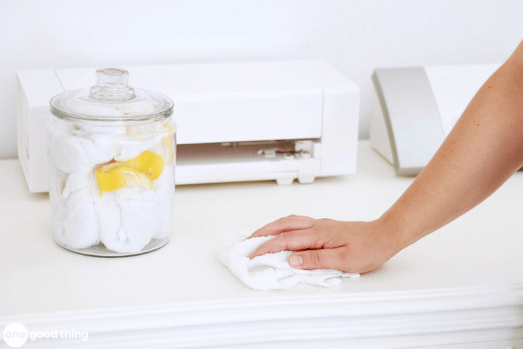 glass jar with lemons and white towels inside sitting on a table with a hand wiping the table with a white towel