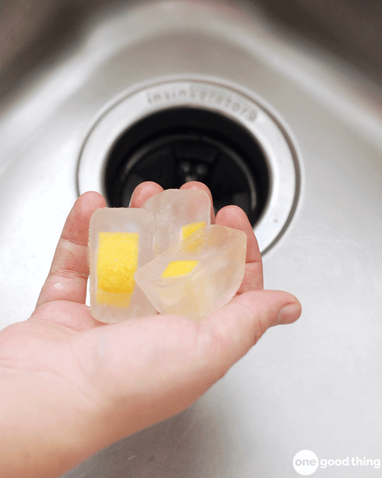 hand holding ice cubes with lemon peels over a stainless steel sink