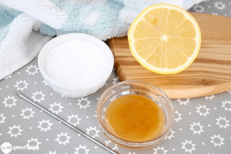 white bowl of baking soda, glass bowl of honey, and half a lemon sitting together on a grey and white floral background