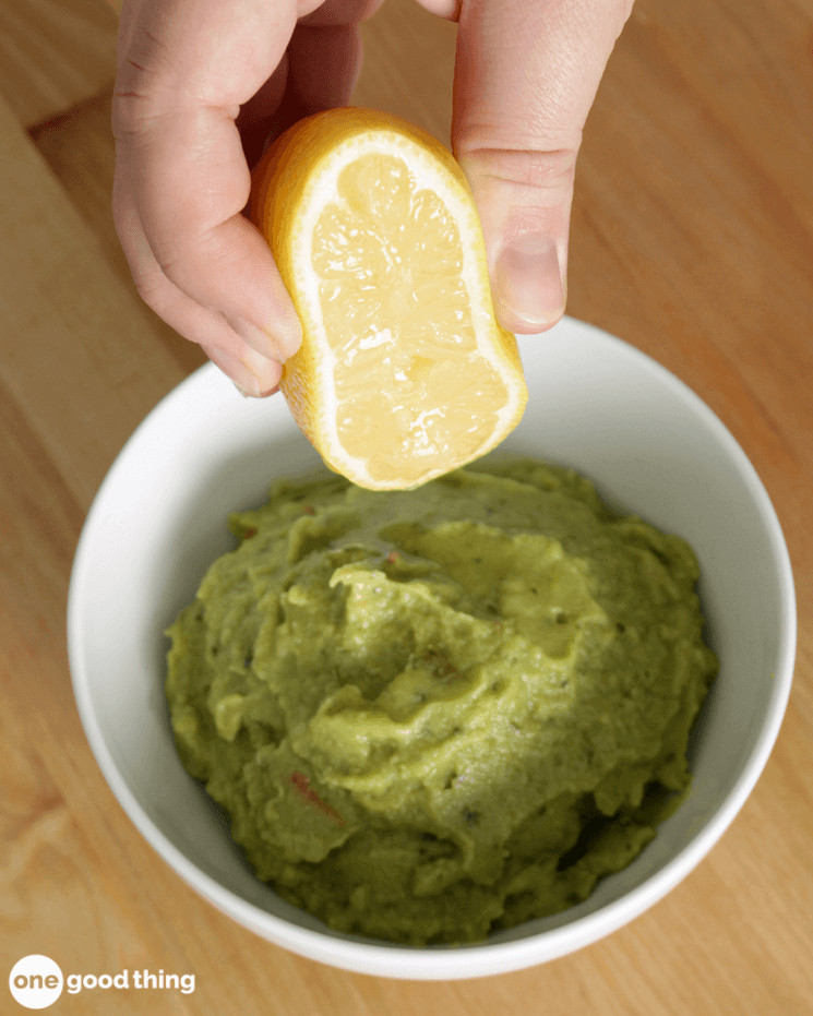 hand squeezing half a lemon onto a bowl of guacamole