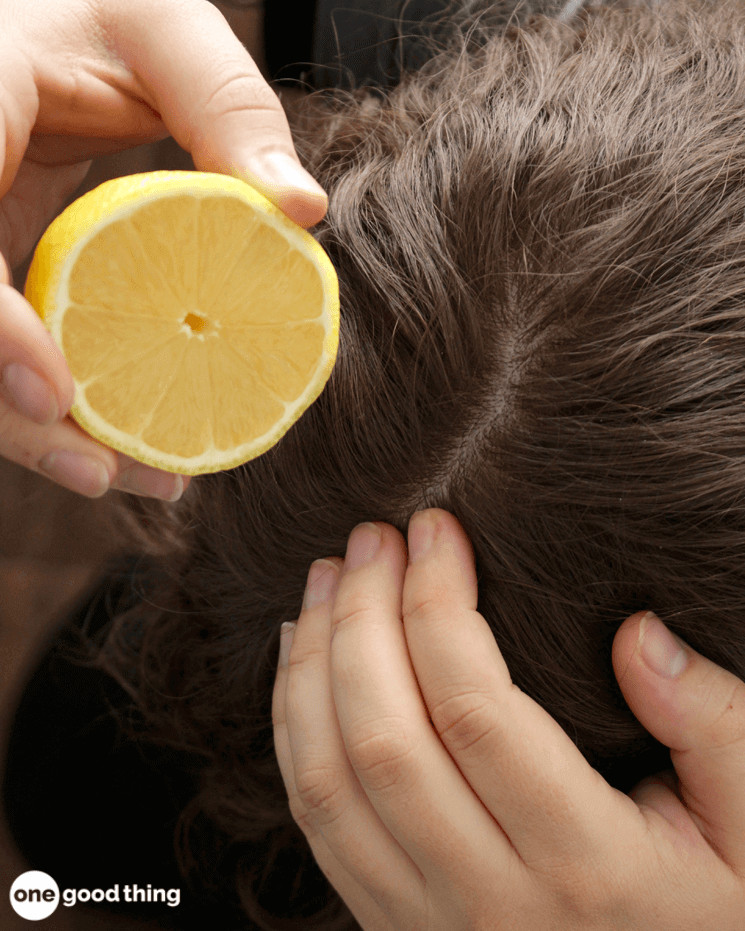 hand squeezing half a lemon onto a head of brown hair