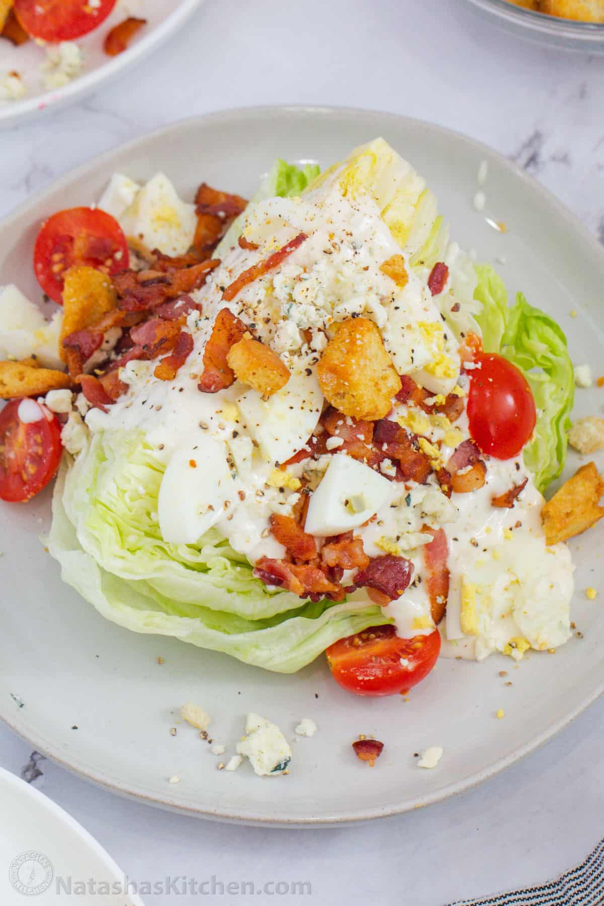 Lettuce wedge topped with dressing and toppings on a plate. 