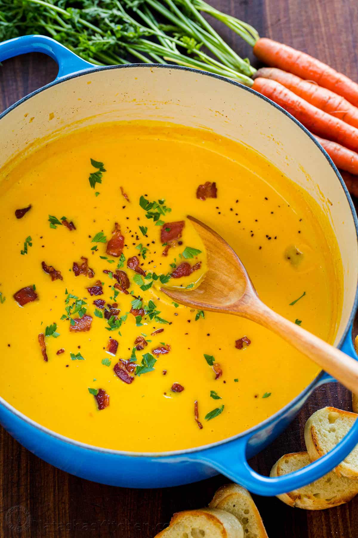 Creamy carrot soup in pot garnished with bacon and parsley