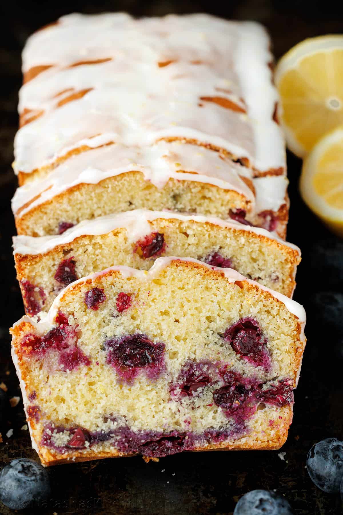 Blueberry Lemon Bread sliced to showcase juicy blueberries cooked throughout each slice, drizzled with lemon glaze