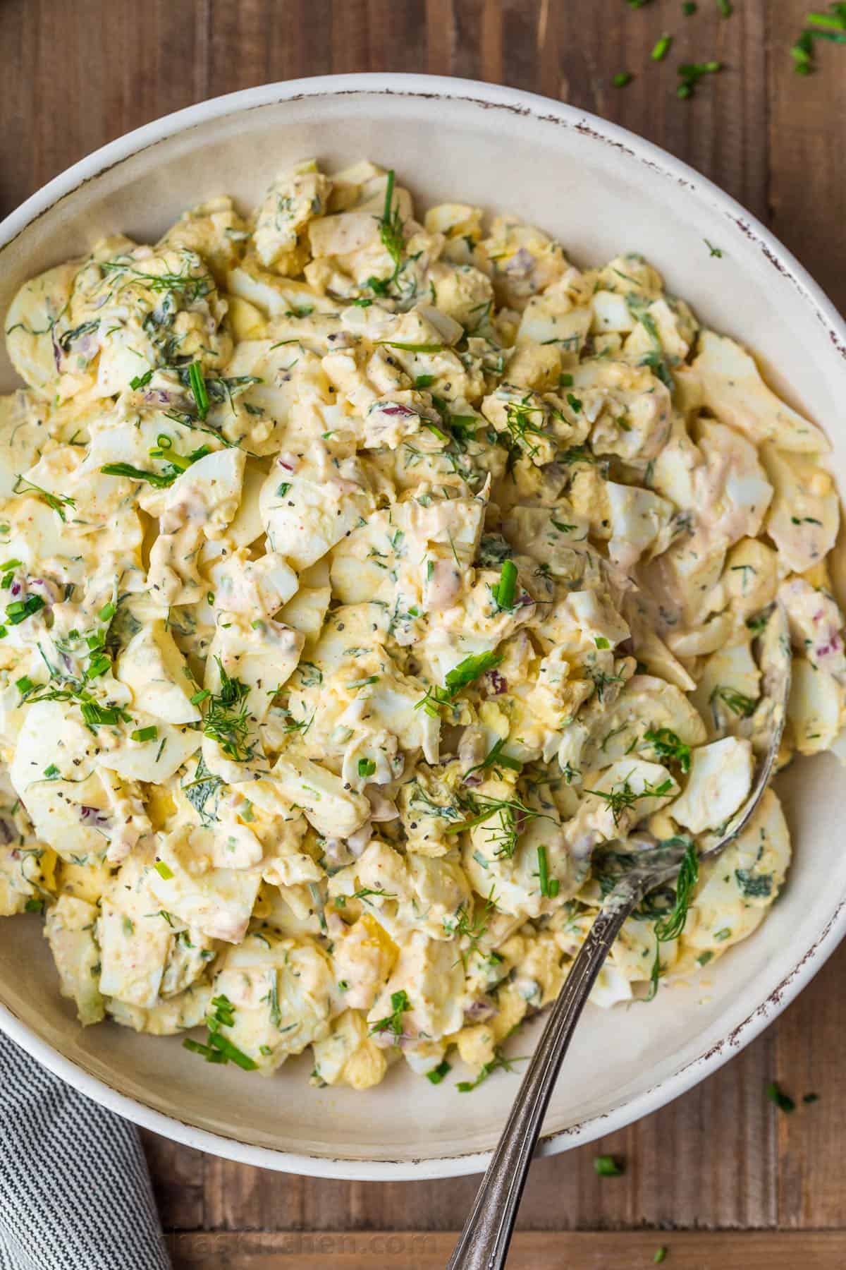 Egg salad in a serving bowl with a spoon and topped with chives.